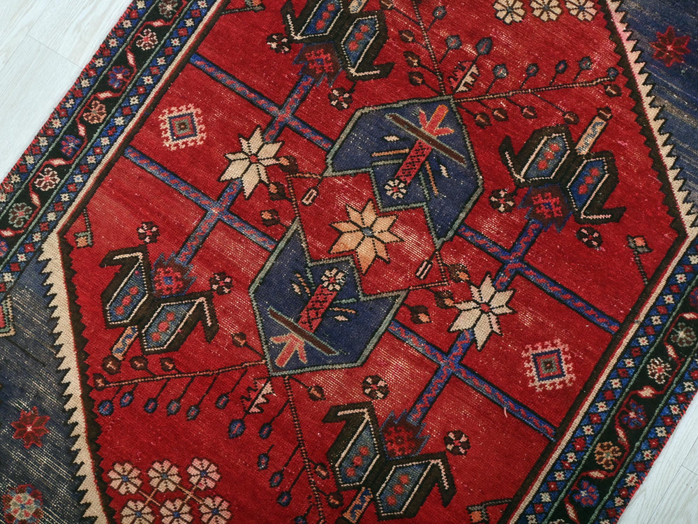a red rug with a blue border on a wooden floor