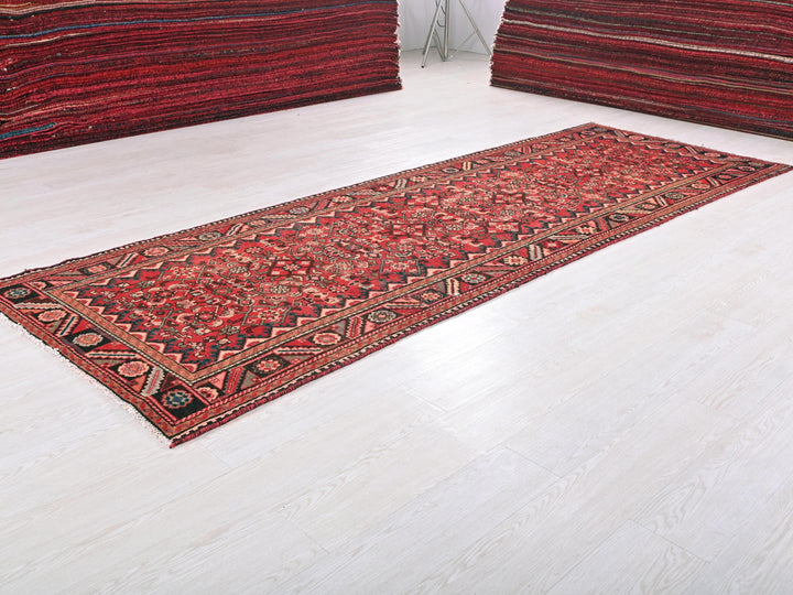 a red rug on a white floor next to a pile of rugs