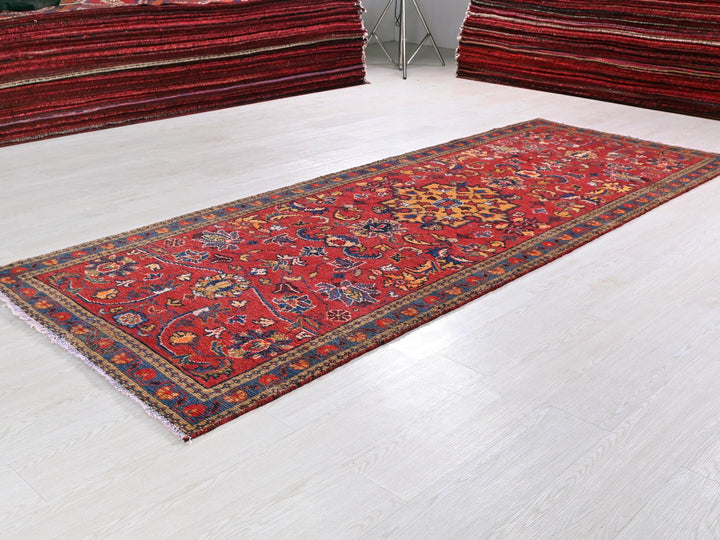 a red rug on a white floor next to a pile of red rugs