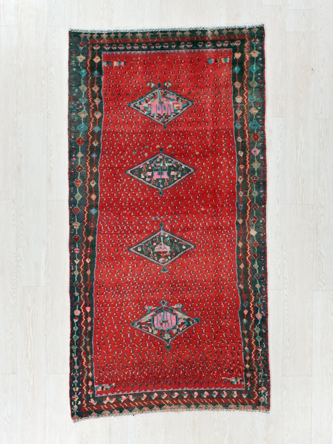 a red rug with a green border on a white floor